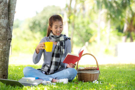 Young people reading book and drinking coffee after working and education on laptop in morning relax at nature garden home. Asia woman meeting conference connect online with office.  Business and Technology Conceptの写真素材