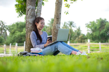Young people work from home with laptop and drinking coffee in morning relax at nature garden home. Asia woman meeting conference connect online with office.  Business and Technology Conceptの写真素材