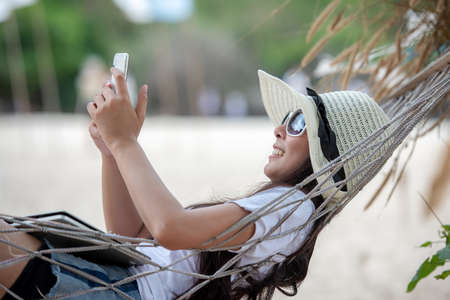 Lifestyle freelance woman using smartphone working and shopping on the beach.Â  Asian people smiling on hammock success and together your  in holiday. Business and Summer Conceptの写真素材