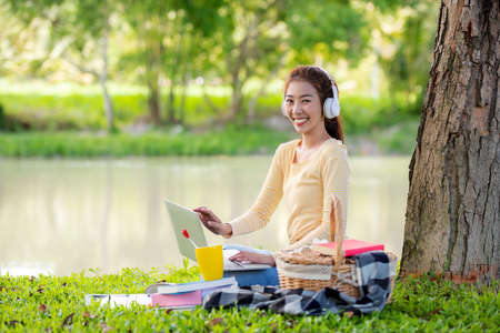 Young people work from home with laptop and drinking coffee in morning relax at nature garden home. Asia woman meeting conference connect online with office.  Business and Technology Conceptの写真素材