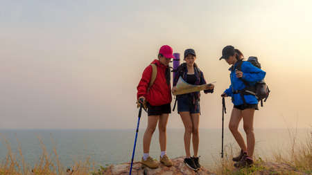 Group asia friends traveler with backpack adventure holding map to find directions and walking relax on mountain near sea outdoor sunset  for destination leisure education nature on vacation. Travel and Lifestyle Conceptの写真素材