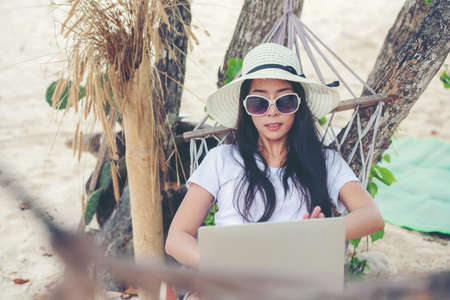 Lifestyle freelance woman using laptop working and relax on the beach.Â  Asian people on hammock success and together your work pastime and meeting conference on internet in holiday. Business and Summer Conceptの写真素材