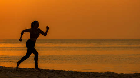 Silhouette athletic woman jogging exercise and relax and freedom on sand beach. People running and workout in sunset background. Lifestyle and Healthy Concept.の写真素材