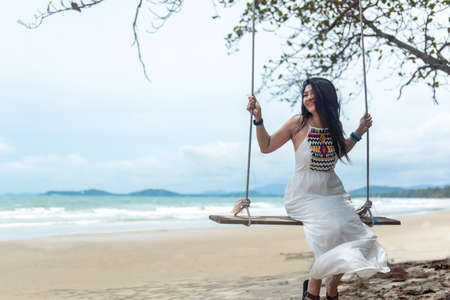 Summer Vacations. Lifestyle women relaxing and enjoying swing outdoors sand beach, fashion stunning women with white dress on the tropical island happy and luxury in holiday summer. Travel and Summerの写真素材