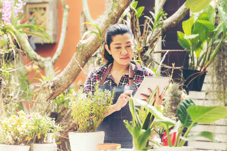 Asian woman care and sale online plant flower in garden. People hobby and freelance gardening indoor at home, nature garden background. Happy and enjoy in spring and summer day.Â  Lifestyle Conceptの写真素材
