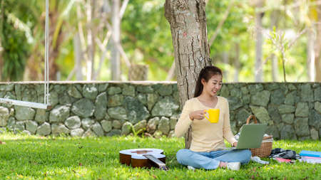 Young people using laptop shopping and leaning education online with drinking coffee in morning relax at nature garden home. Asia woman picnic relax and chill on summer holiday.  Lifestyleの写真素材