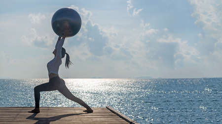 Healthy woman lifestyle balanced practicing meditate and zen energy yoga ball outdoors on the bridge in morning the sea nature. Healthy life Concept.の写真素材