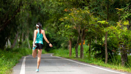 Healthy woman warming up before jogging run and relax stretching her arms and looking away in the road outdoor. Asian runner people workout fitness session, nature park background. Healthy and Lifestyle Conceptの写真素材