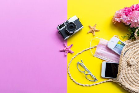 Traveler accessories medical face mask , hand gel sanitizer protect virus in hand bag, pink yellow background. Tourism backpack and visiting for planning airplane trips travel destination and vacations. Top view and copy space for text.の写真素材