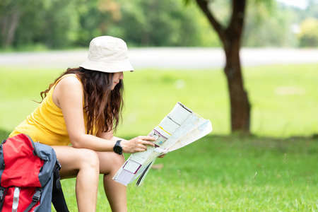 Women hiker or traveler with backpack adventure holding map to find directions and siting relax in the jungle forest outdoor for destination leisure education nature on vacation. Travel and Lifestyle Conceptの写真素材