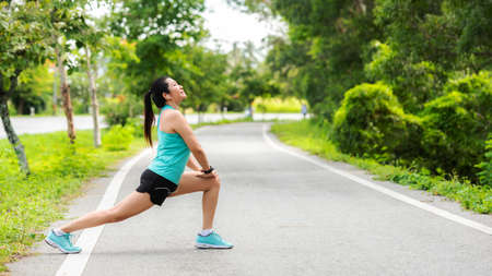 Healthy smiling woman warming down stretching her legs and looking away in the road outdoor. Asian runner woman workout before fitness and jogging session at the park. Health care Lifestyle Concept.の写真素材