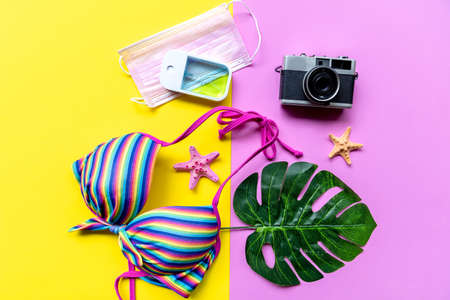 Traveler accessories medical face mask , hand gel sanitizer protect with bikini, pink yellow background. Tourism backpack and visiting for planning trips travel destination and vacations. Top viewの写真素材