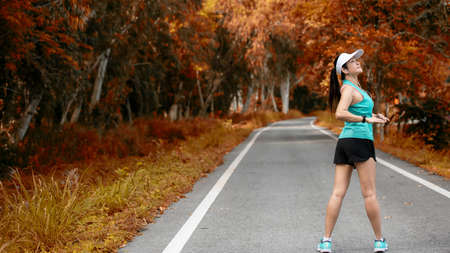 Healthy woman warming down stretching her legs and looking away in the road outdoor. Asian runner woman workout before fitness and jogging session at the park. Health care Lifestyle Concept.の写真素材
