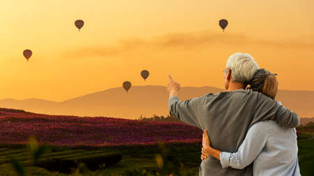 Asian Lifestyle senior couple hug and pointing balloon on mountain with field cosmos in sunrise nature.  Old people happy in love romantic and relax time.Â  Tourism family elderly retirement travel in attraction place tourist travel leisure and destination.の写真素材