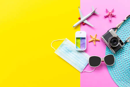 Traveler accessories medical face mask , hand gel sanitizer protect  in hand bag, pink yellow background. Tourism backpack and visiting for planning airplane trips travel destination and vacations. Top view and copy space for text.の写真素材