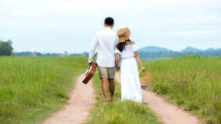 Lifestyle couple picnic sunny time. Asian young couple having fun and walking relax in the meadow and field in holiday.  Romantic and In love.   Lifestyle conceptの写真素材