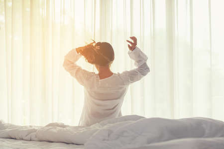 Asian women waking up stretching and raise arms in bed room at home. Young people early morning time and sunny day. Lifestyle Conceptの写真素材