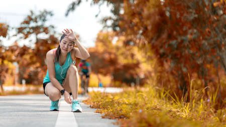 Running woman tying laces of running shoes before jogging through the road in the workout autumn nature park.  Jogger tire after running.  Weight Loss and Healthy Conceptの写真素材