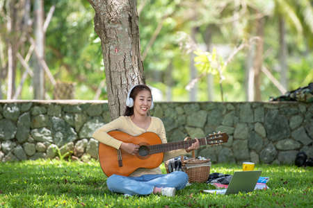 Young people playing guitar and drinking coffee after working and education on laptop in morning relax at nature garden home. Asia woman beauty and smiling chill and enjoy in summer holiday.  Lifestyle Conceptの写真素材
