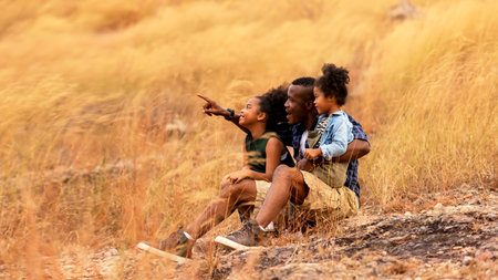 Happy African family father and child daughter travel and sitting pointing on meadow nature on silhouette lights sunset.  Travel and Family Conceptの写真素材