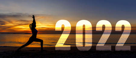 Happy new year card 2022. Silhouette lifestyle woman yoga practicing yoga standing as part of Number 2022 near the beach at sunset. Healthy and Holiday Conceptの写真素材