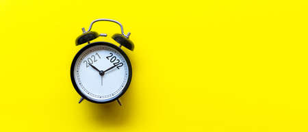 2021 and 2022 on black alarm clock on yellow background.  Merry Christmas and Happy new year concept. Copy space and banner for textの写真素材