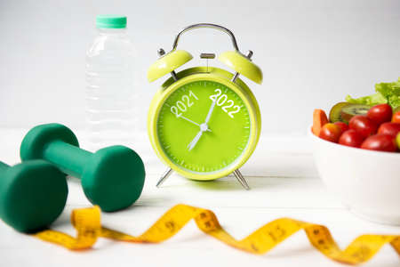 2021 and 2022 on alarm clock with workout planing for dieting. Sport exercise equipment workout andÂ gym nutrition fresh salad for fitness. Merry Christmas and Happy new year conceptの写真素材