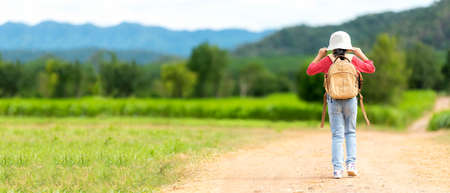Children girl travel nature summer trips. Asia people kid tourism walking on road nature meadow,  happy and fun explore adventure camping outdoors for leisure and destination, mountain background. Travel Lifestyle Concept, copy space for bannerの写真素材