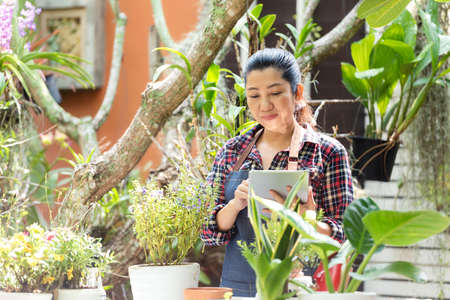 Asian woman care and sale online plant flower in garden. People hobby and freelance gardening indoor at home, nature garden background. Happy and enjoy in spring and summer day.Â  Lifestyle Conceptの写真素材