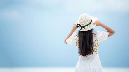 Summer vacations. Lifestyle woman relax and chill on beach.  Asian happy young people wearing white dress fashion and holding hat in summer trips enjoy  tropical beach. Lifestyle and Travel Concept.の写真素材