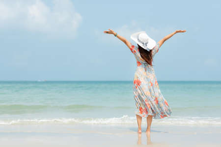 Summer vacations. Lifestyle woman relax and chill on beach background.  Asia happy young people with white dress raise arm on the wave sea, summer trips walking enjoy  tropical beach. Lifestyle and Travel Concept.の写真素材