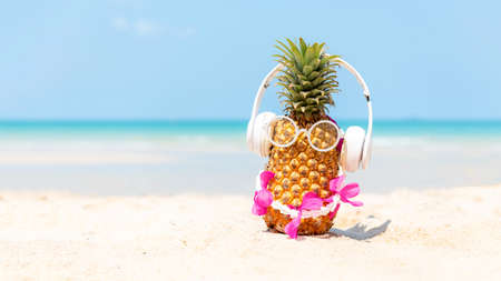 Summer in the party.  Hipster Pineapple Fashion in sunglass and listen music with sunblock and sandal on the sand beach beautiful blue sky background.  Creative art fruit for tropical style.   Fashion Summer Vacation Conceptの写真素材