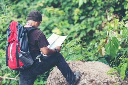 Tourism asian lifestyle man and traveler with backpack adventure holding map to find directions in the jungle forest destination and leisure outdoor for education nature. Travel and Trips Conceptの写真素材