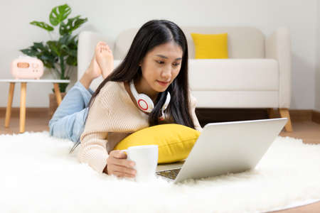 Young smiling woman happy watching movies and  chill relax in summer holiday. Lifestyle girl using laptop for entertainment in living room at home.  Lifestyle Conceptの写真素材