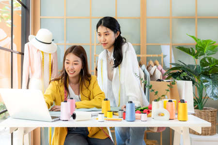 Two Young women fashion designer using laptop working and received order customer for design tailor and cloth in the showroom,  Lifestyle Stylish tailor taking measurements on mannequin for cutting cloths in studio.  Business SME and Industry small Conceptの写真素材