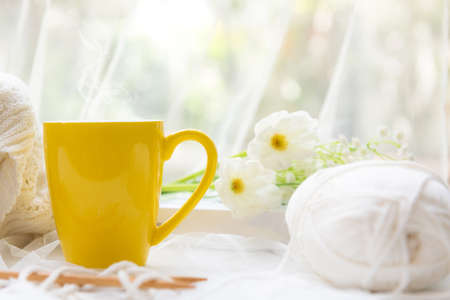 Coffee morning.  Yellow steaming cup of hot coffee for relax after working hobbies crochet on white wooden near window with flowers.の写真素材