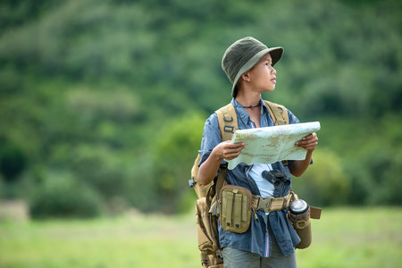 Asian boy backpack checking map and pointing in jungle forest, trips adventure and tourism for destination leisure for education and relax in nature park .  Travel vacations Conceptの写真素材