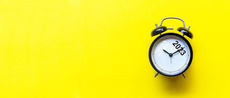 2022 and 2023 on black alarm clock on yellow background, Merry Christmas and Happy new year concept. Copy space and banner for textの写真素材