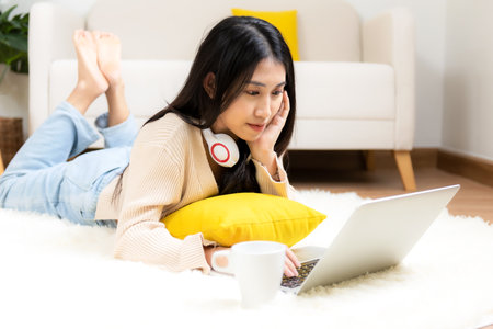 Young smiling woman happy watching movies and  chill relax in summer holiday. Lifestyle girl using laptop for entertainment in living room at home.  Lifestyle Conceptの写真素材