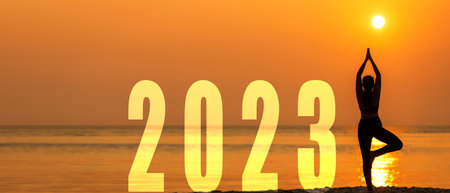 Happy new year card 2023. Silhouette lifestyle woman yoga practicing yoga standing as part of Number 2023 near the beach at sunset. Healthy and Holiday Conceptの写真素材
