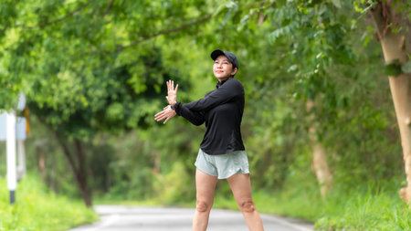 Healthy woman warming up before jogging run and relax stretching her arms and looking away in the road outdoor. Asian runner people workout fitness session, nature park background. Healthy and Lifestyle Conceptの写真素材