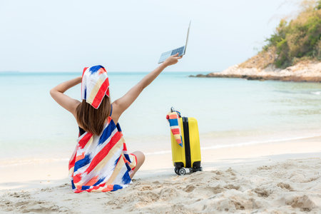 Lifestyle freelance woman raise arms relax after using laptop working on the beach. Asian people success and together your work pastime and meeting conference on internet in holidayの写真素材