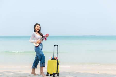 Summer vacations. Lifestyle young woman play guitar  relax and chill.  Asia happy young people standing near the wave sea, summer trips enjoy tropical beach. Lifestyle and Travel Conceptの写真素材