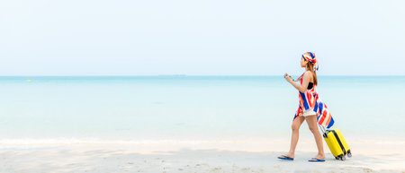 Summer vacations. Lifestyle  woman relax and chill on beach background.  Asia happy young people walking with bag travel suitcase luggage fashion dress.  Summer trips travel, copy space for bannerの写真素材