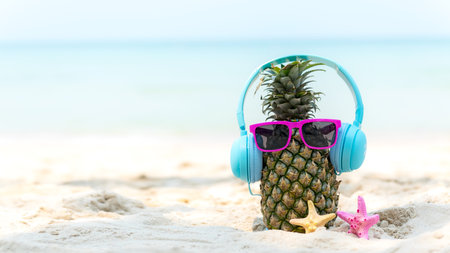 Summer in the party.  Hipster Pineapple Fashion in sunglass and listen music with sunblock and sandal on the sand beach beautiful blue sky background.  Fashion Summer Vacation Concept, copy space for bannerの写真素材