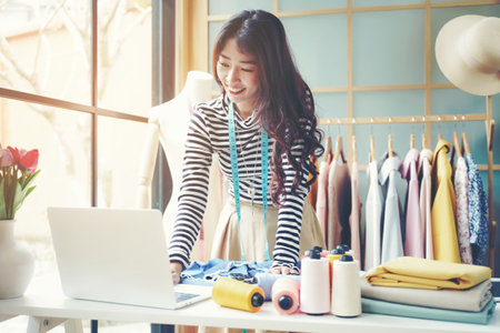 Young women fashion designer using laptop working and received order customer for design tailor and cloth in the showroom,  Lifestyle Stylish tailor taking measurements on mannequin for cutting cloths in studio.  Business SME and Industry small Conceptの写真素材