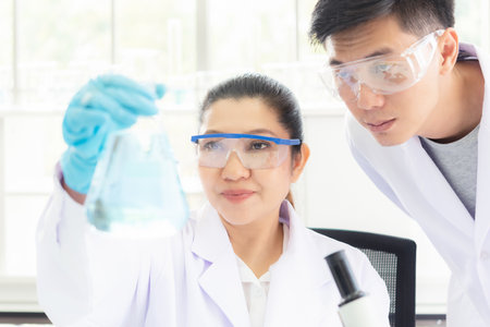 Team work asian woman and man Scientists analyzing study data and evaluating microscope success for work shop. Health care researchers doing some research with dropper chemical testing in life science laboratoryの写真素材