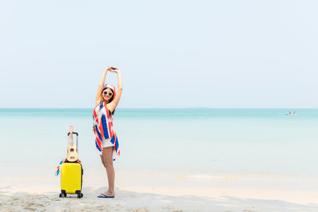 Summer vacations. Lifestyle  woman relax and chill on beach background.  Asia happy young people with bag travel suitcase luggage fashion dress raise arm wave sea, summer trips travelの写真素材