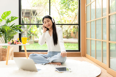 Young smiling woman happy listen music for chill and relax in summer holiday. Lifestyle girl using laptop for entertainment in living room at home.  Nature garden background.  Lifestyle Conceptの写真素材