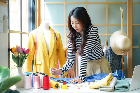 Asian young women fashion designer  working on her designer in the showroom,  Lifestyle Stylish tailor use computer clothing design in studio.  Business small Conceptの写真素材